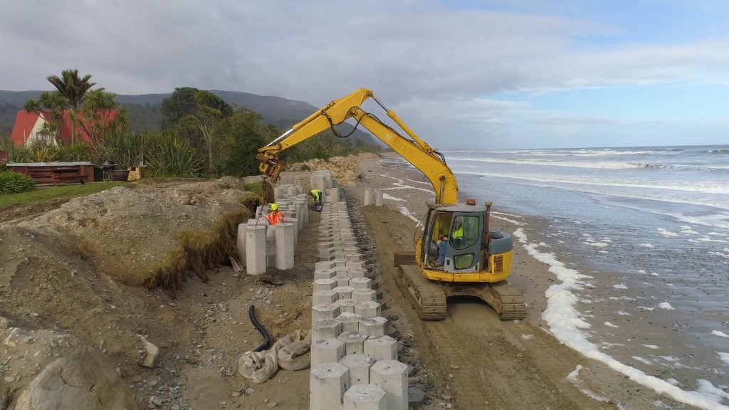 Machinery on the beach line lifting heavy concrete blocks in line with the concrete wall